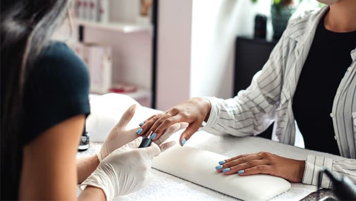 En nagelterapeut applicerar ljusblått nagellack på en kund under en manikyr.