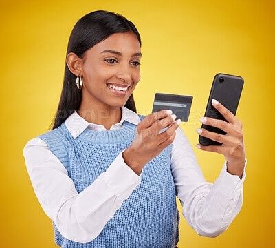 Kvinna håller ett betalkort och en mobiltelefon mot gul bakgrund